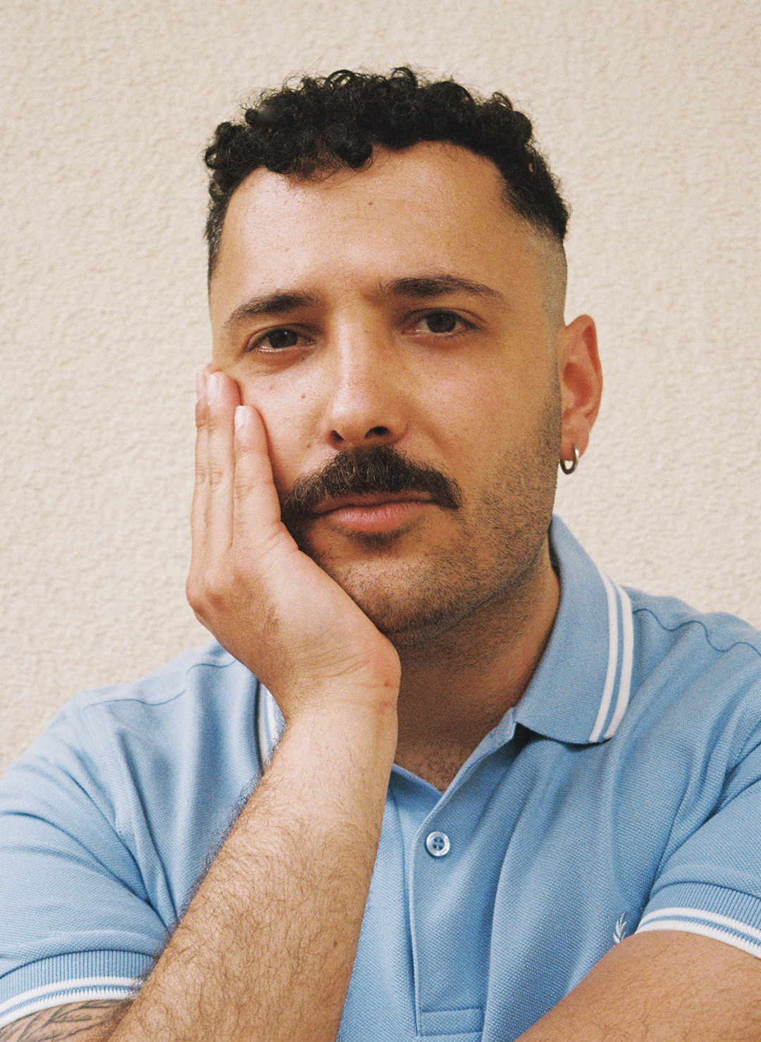 Portrait von Fikri Anıl Altıntaş vor einer Wand. Er schaut in die Kamera und stützt sein Gesicht auf seiner rechten Hand ab.